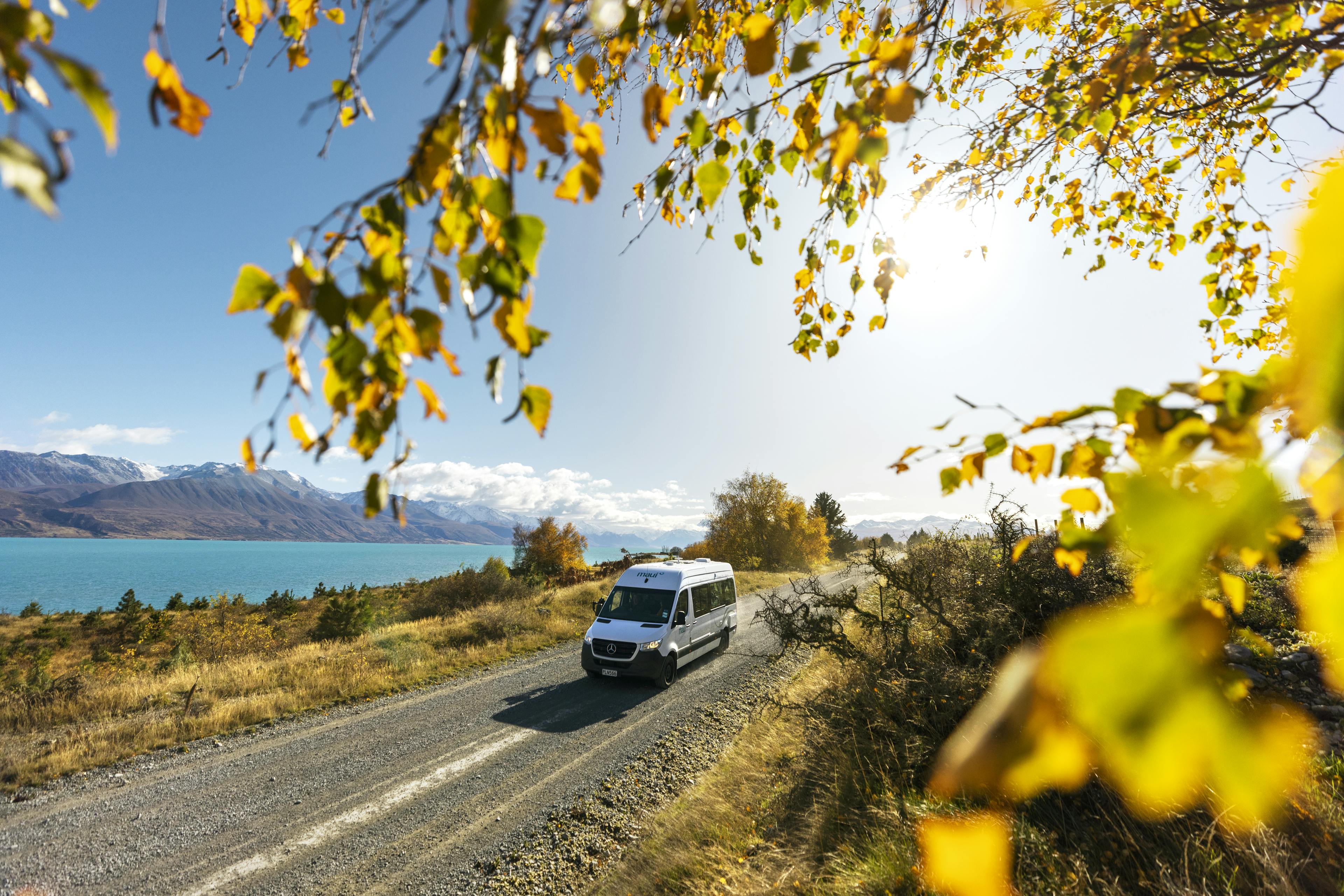 A campervan on a beautiful road near a lake in autumn