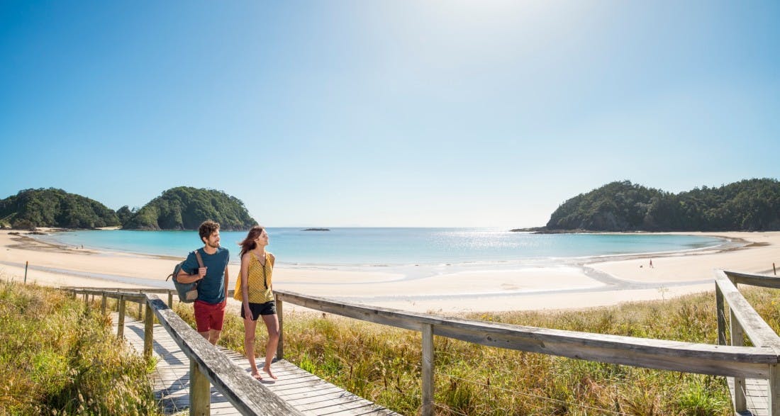 Two tourists walking on the beach at Matapouri in Northland
