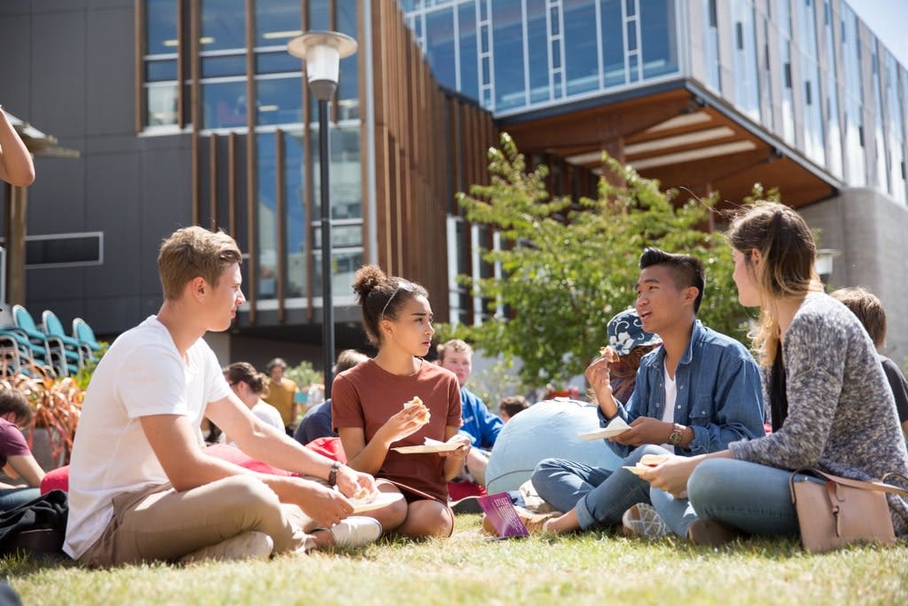 A group of students sitting on the lawn and talking on campus