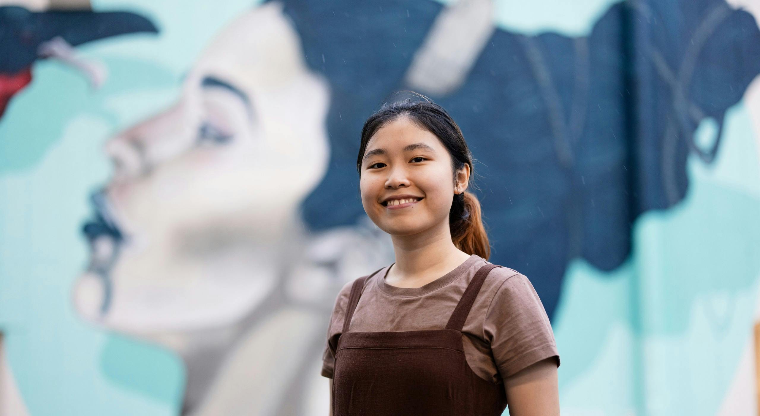 Vietnamese student smiling into the camera in front of a mural. 