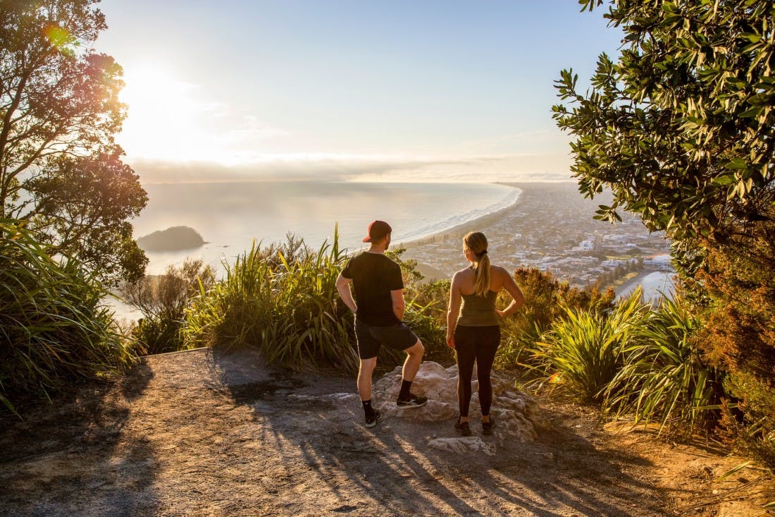 Two tourists standing at the top of Mount Manganui overlooking the view in Tauranga